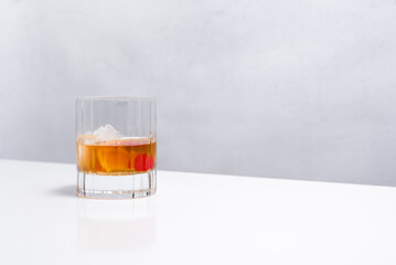 Vaso de vermut rojo con hielo decorado con cerezas y rodajas de naranja sobre mesa blanca	