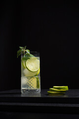 Un vaso de refrescante cóctel de jugo de lima con rodajas de lima y hielo sobre fondo negro	
