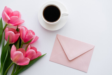 top view of bouquet of tulips near cup of coffee and pink envelope on white.