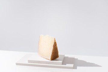 Trozo de queso curado manchego de oveja sobre mesa blanca y fondo claro. Aperitivo español