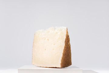 Trozo de queso curado manchego de oveja sobre mesa blanca y fondo claro. Aperitivo español