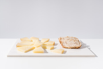 Trozos de queso manchego de oveja curado con tostadas de pan crujiente sobre una mesa blanca. Tapas españolas