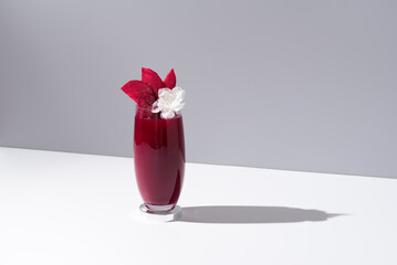 Un vaso de jugo de remolacha decorado con rodajas de remolacha sobre una mesa blanca y fondo gris	