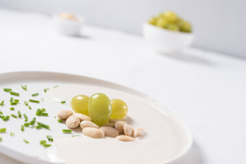 Crema de almendras, sopa fría española. Ajo blanco de Málaga con almendras y uvas en un recipiente blanco sobre una mesa blanca