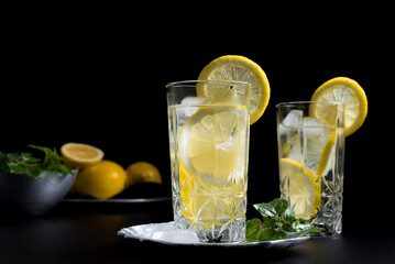 Dos vasos de refrescante zumo de limón, cóctel de frutas con rodajas de limón y hielo sobre fondo negro	