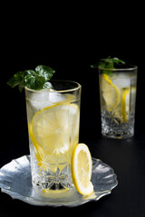 Dos vasos de refrescante zumo de limón, cóctel de frutas con rodajas de limón y hielo sobre fondo negro	