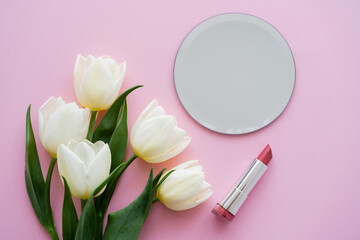 top view of white tulips near mirror and lipstick on pink.