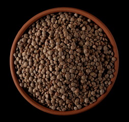 Brown uncooked lentils in clay pot isolated on black