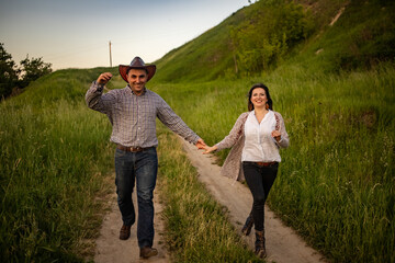 a couple in love runs holding hands along the road in the village. Guy in a cowboy hat