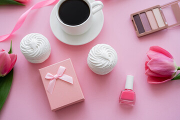 top view of gift box, zephyr, decorative cosmetics and tulips near cup of coffee on pink.