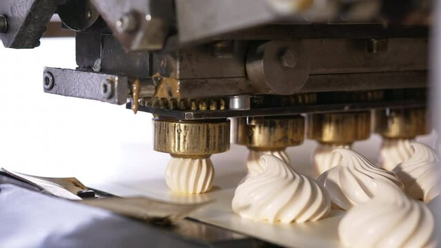Few metal nozzles rotate and squeeze creamy marshmallows on conveyor belt. Automated line for desserts manufacturing. Close up.