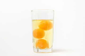 Broken raw chicken eggs in a glass on a white background. Chicken egg yolk. Drinking raw chicken eggs