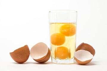 Broken raw chicken eggs in a glass on a white background. Chicken egg yolk. Drinking raw chicken eggs