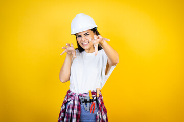 Young caucasian woman wearing hardhat and builder clothes over isolated yellow background smiling...