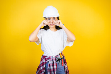 Young caucasian woman wearing hardhat and builder clothes over isolated yellow background depressed...
