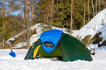 Blue down sleeping bag to dry on a green tent in the winter forest.