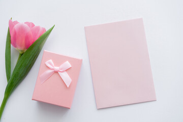 top view of envelope near gift box and pink tulip on white.