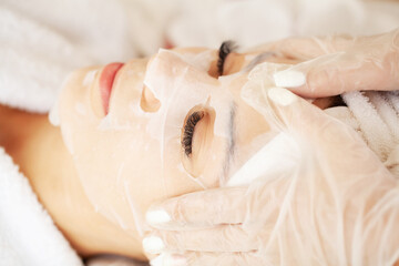 Cosmetologist applying sheet mask on woman in spa salon