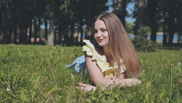 A beautiful girl poses lying on the grass in the park.