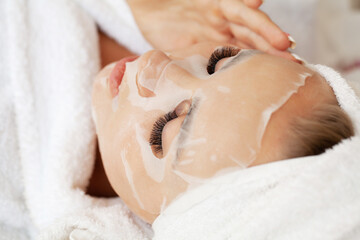 Cosmetologist applying sheet mask on woman in spa salon