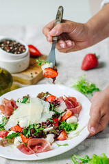 Salad mix with jamon, baby mozzarella, strawberries and vinaigrette sauce. Woman tasting salad with a fork