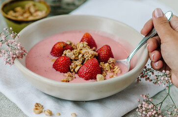 A woman pours homemade granola into a bowl of strawberry yogurt. Healthy breakfast concept.