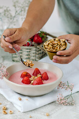A woman pours homemade granola into a bowl of strawberry yogurt. Healthy breakfast concept.
