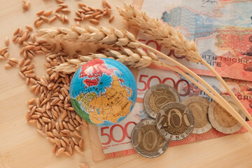 Ears of wheat, grain next to a globe in miniature and banknotes of Kazakhstan, 5000 tenge with...