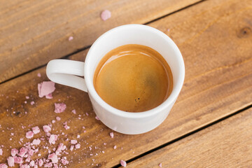 Espresso coffee on a wooden table. Coffee in a small cup. Good morning. Coffee on the table with pink crumbs.
