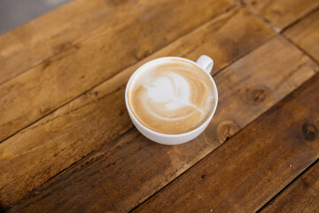 Woman holding latte art coffee on wooden table in coffee shop. Coffee in a mug.