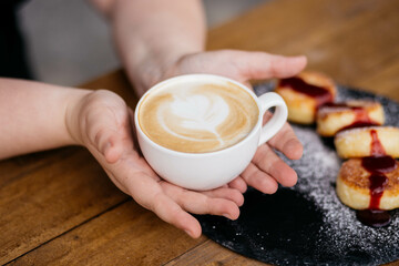 Woman holding latte art coffee on wooden table in coffee shop. Coffee in a mug.