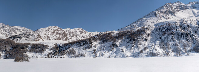 steep rocky slopes and Stampa village on frozen mountain lake, from Plaun da Lej, Switzerland