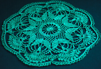 Beautiful knitted napkin on  dark green background. Green lace knitted fabric. Handmade items. texture is knitted from threads.