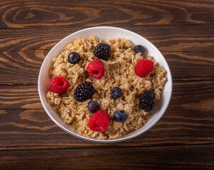Oatmeal with berries in a bowl on wooden background