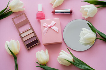top view of white flowers, gift box and decorative cosmetics on pink.