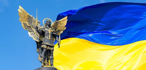 Fotobehang Standbeeld van een engel op het Onafhankelijkheidsplein in Kiev. Aartsengel Michaël is de hemelse beschermheer van Kiev. Grote vlag van Oekraïne op de achtergrond. Russische oorlog in Oekraïne. © Valentin Kundeus