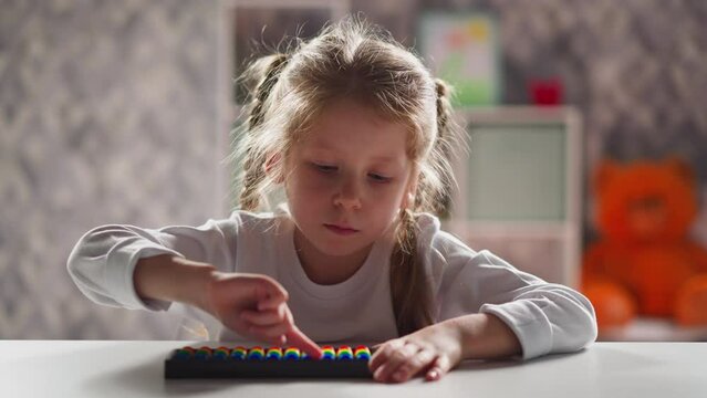 Thoughtful little kid with blonde plaits touches colorful abacus beads by finger during mental arithmetic lesson close view slow motion