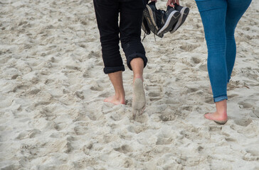 Couple with bare foot holding shoes walking on a sandy beach