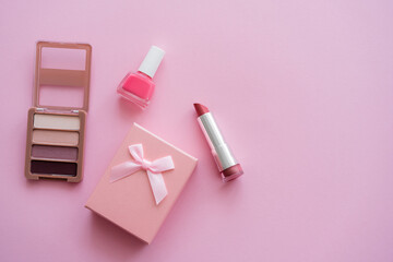 Obraz na płótnie Canvas top view of decorative cosmetics near present with bow on pink.