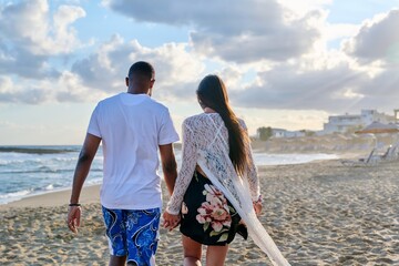 Young happy couple walking on the beach holding hands, back view.