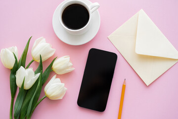 top view of white tulips near smartphone with blank screen and cup of coffee on pink.