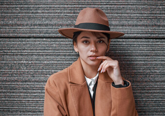Young business lady in retro style on background of stone wall in brown-beige coat and classic hat, isolated portrait in natural light