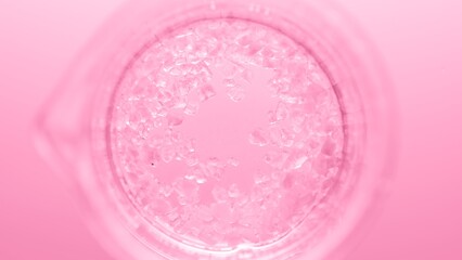 Top view macro shot of crystals in clear fluid in flask creating different sized bursting bubbles on pink background | Mineral skincare cosmetics formulating concept
