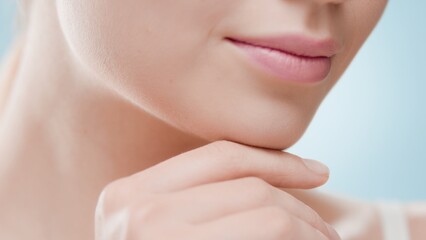 Obraz na płótnie Canvas Extreme close-up of female beauty model with perfect skin touches her chin against blue background | Face care commercial concept