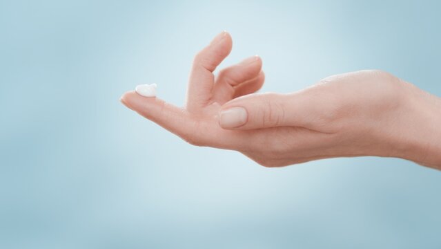 Female hand with a drop of skin care cream on forefinger against blue background | Skin care cream commercial concept