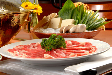 Shabu-shabu dish with vegetables, noodles, sauces, tofu and fondue burner on wooden table