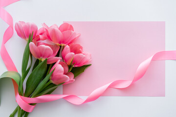 top view of bouquet with tulips near ribbon and pink paper on white.