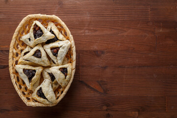 Gomentash with poppy seeds and prunes freshly baked for the Purim holiday on a wooden table in a wicker bread basket.copy space.
