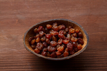 Raisins in a bowl of coconut shell on a wooden table.