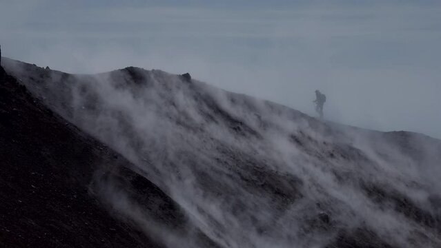 Silhouette of man hiking at coldera of Avachinsky stratovolcano, also known as Avacha Volcano. Backpacker tourist moves upon rocks behind steam from hot geysers. Kamchatka Peninsula, Russia.